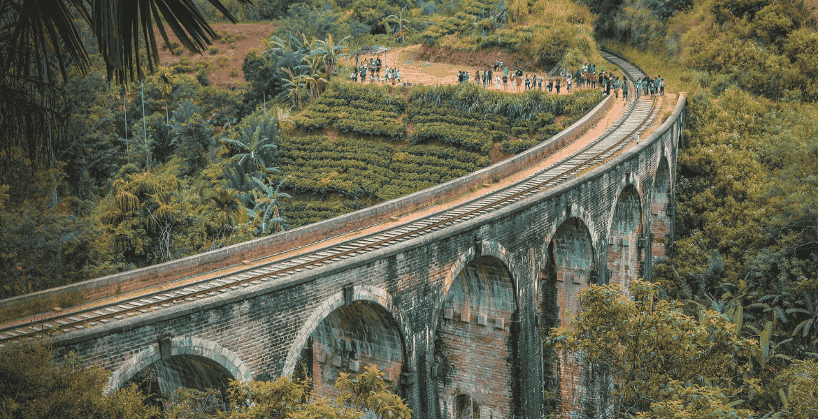 Scenic view of the Nine Arches Bridge in Ella, Sri Lanka, surrounded by lush tea gardens and curving railway tracks through the hill country.