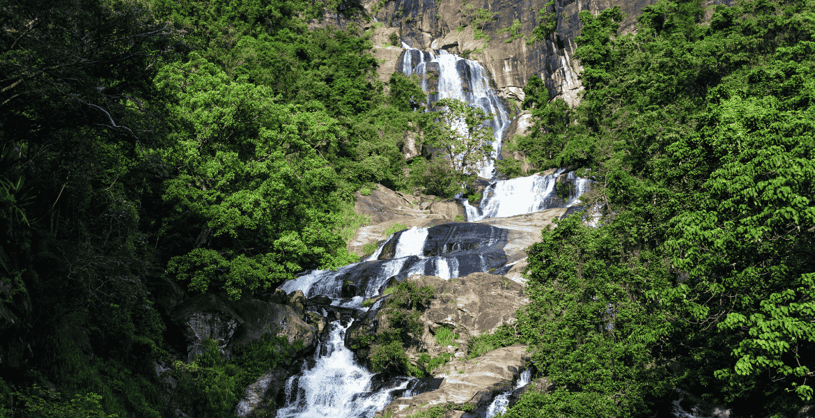 Ravan Ella Waterfall cascading over high rocks, surrounded by lush green forest and bushes in Ella, Sri Lanka.